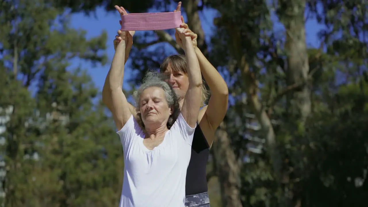 Focused elderly lady with personal trainer in summer park