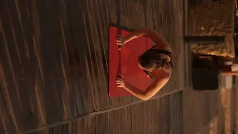 Vertical video a brunette girl doing push-ups on a red mat on the beach covered with black boards Front view of a brunette girl while doing sports