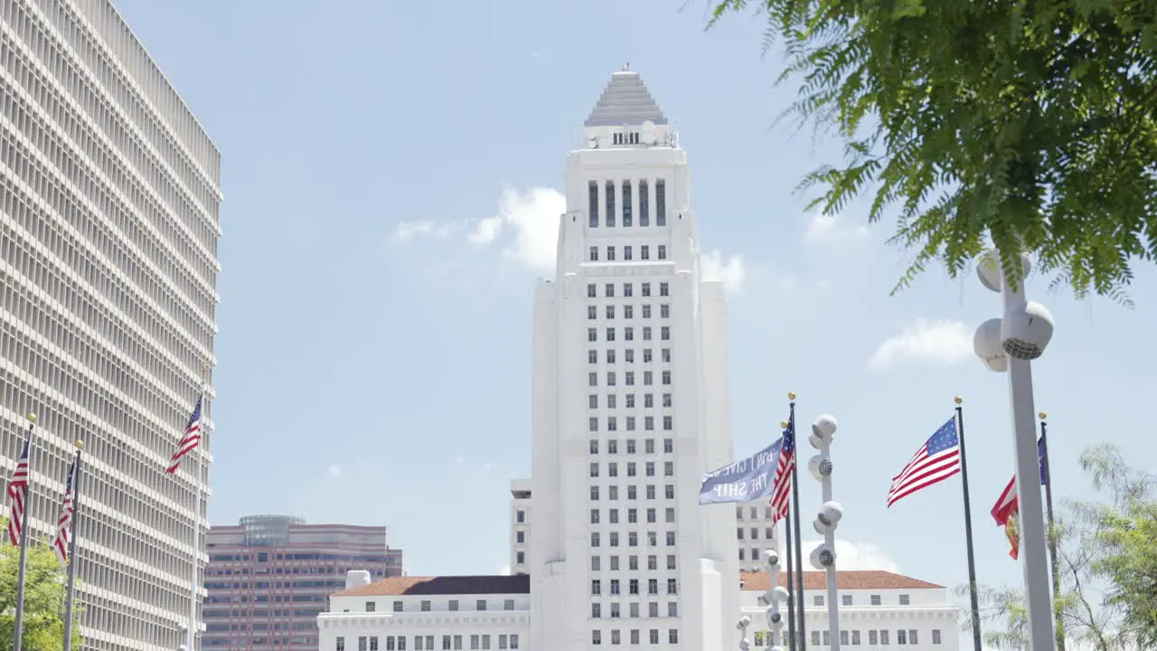 View onto the city hall of Los Angeles near while airplane passing near Clara Shortridge Folz Criminal Justice center of the Gloria Monila Grand Park during summer time american flags in front steady