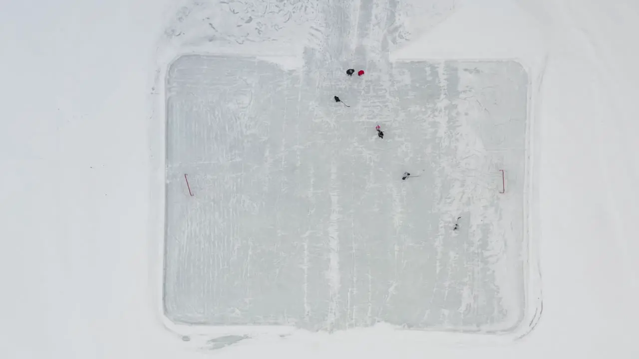 Aerial top down people playing ice hockey on small outdoor rink on frozen lake