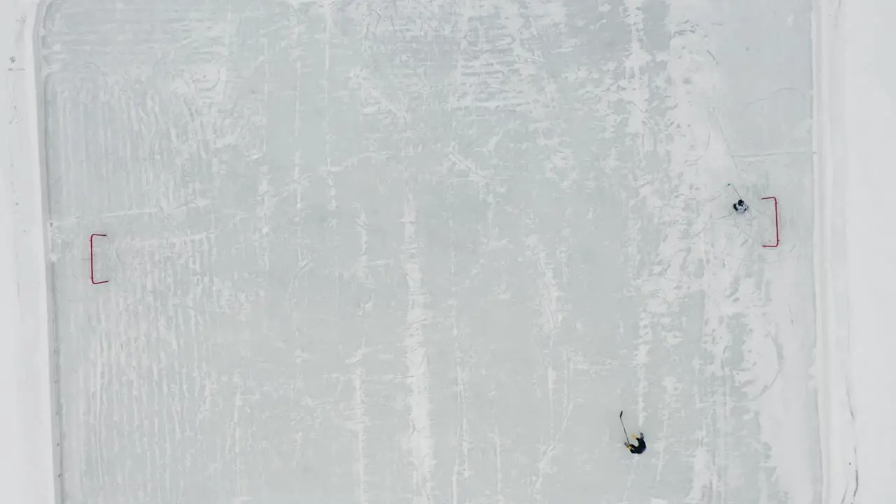 Aerial top down two people playing ice hockey on small ice rink on frozen lake