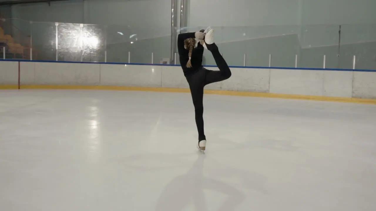 Slow motion footage of a young girl dressed in black figure skating in an ice arena