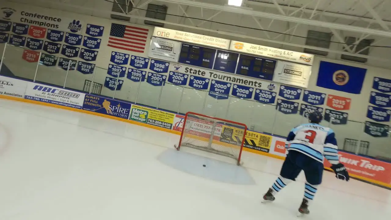 FPV drone ice hockey player skating down arena rink shooting puck into goal