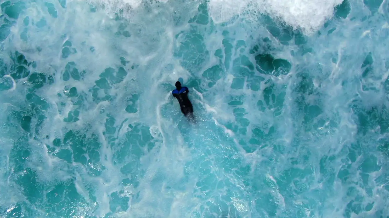 AERIAL  Birdseye view of surfer battling the waves current and white wash in a turbulent ocean