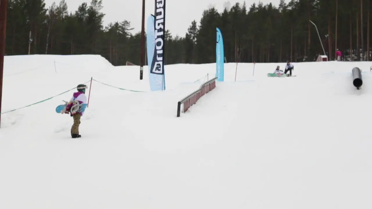 Snowboard Girl Kid walking up the Slope with her Snowboard on her back at a Competition