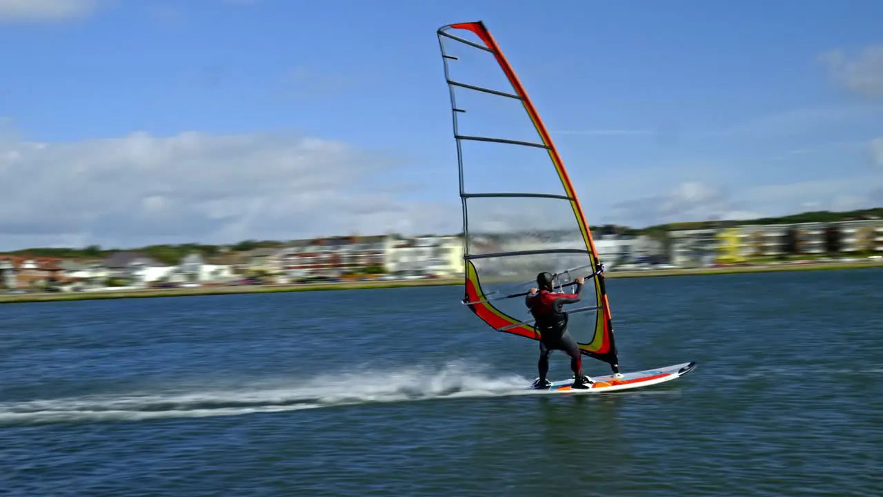 Windsurfer blown along by strong sea breeze balances on his surf board at West Kirby marine lake