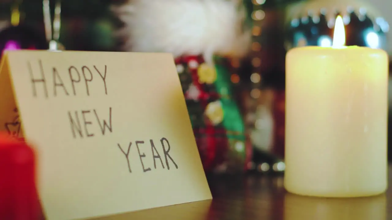 Greeting card saying "Happy New Year" with candles and Christmas tree and decorations around it