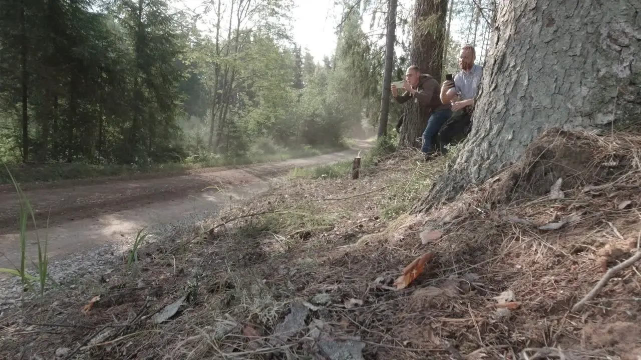 WRC raly spectators film on their phones how fast rally car fly s bye on high speed on gravel road surrounded by forest dust cloud is seen in sunlight