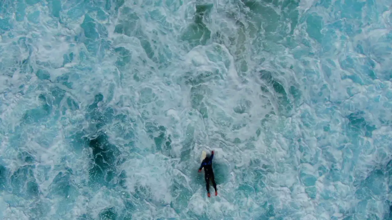 AERIAL Birdseye view of surfer battling the waves current and white wash in a turbulent ocean