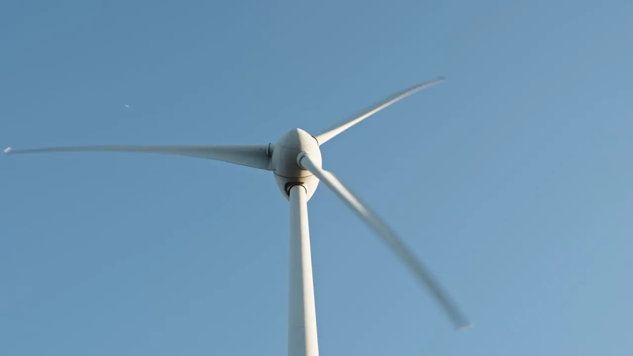 Wind turbine rotating against a clear blue sky symbolizing sustainable energy and technology