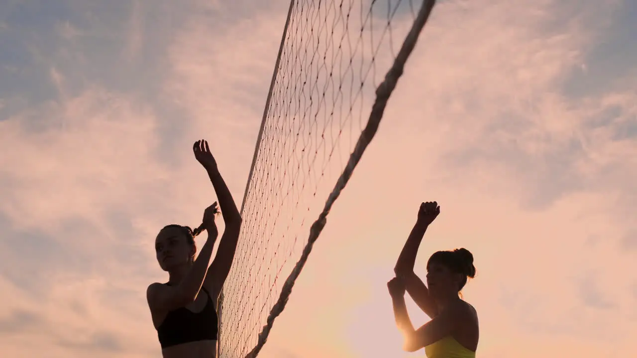 Sexy girls volleyball players pass the ball near the net and hit the ball at sunset in slow motion