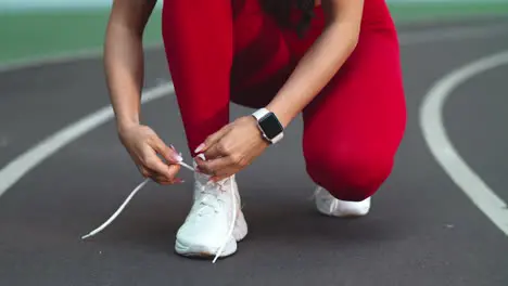 Close up of fitness woman lacing up footwear for marathon on track