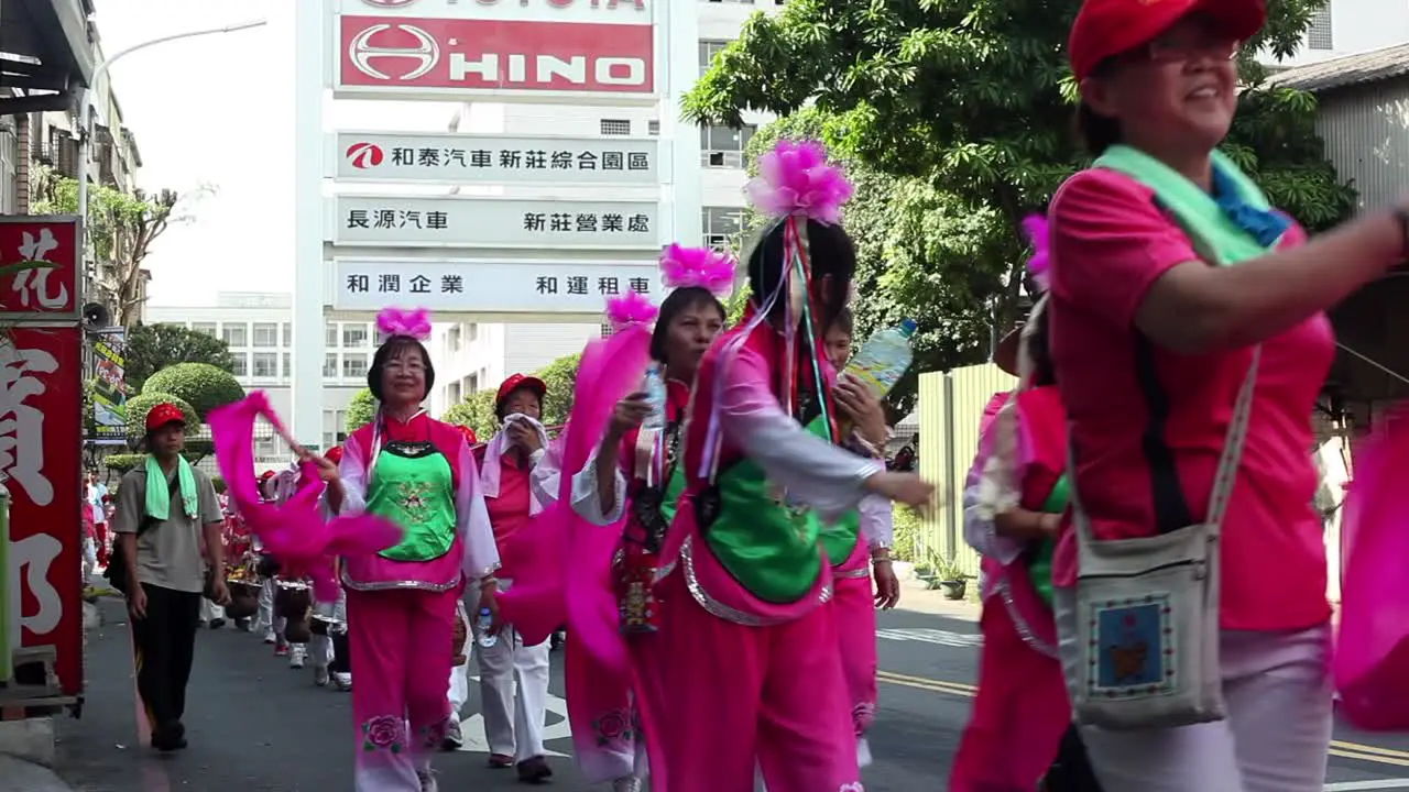 Asian dancers waving large pink ribbons during street parade