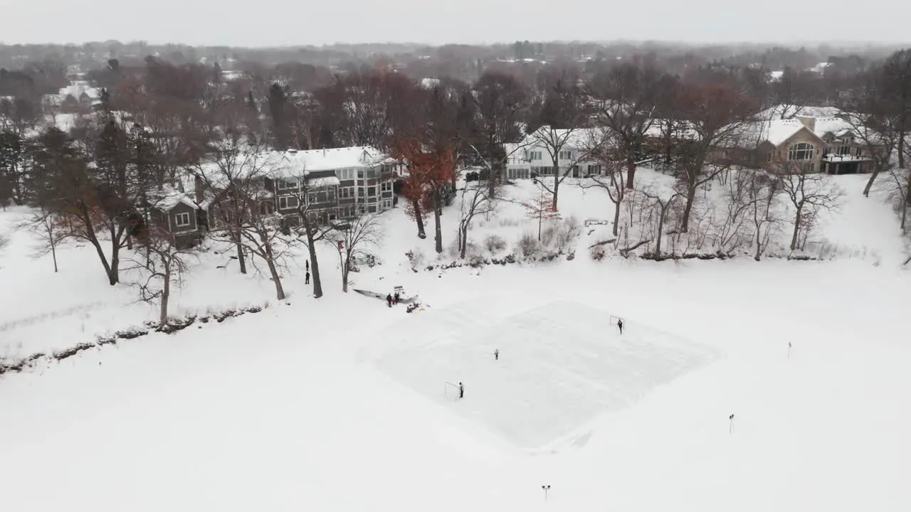 Aerial of a family playing ice hockey in their backyard homemade rink while snowing