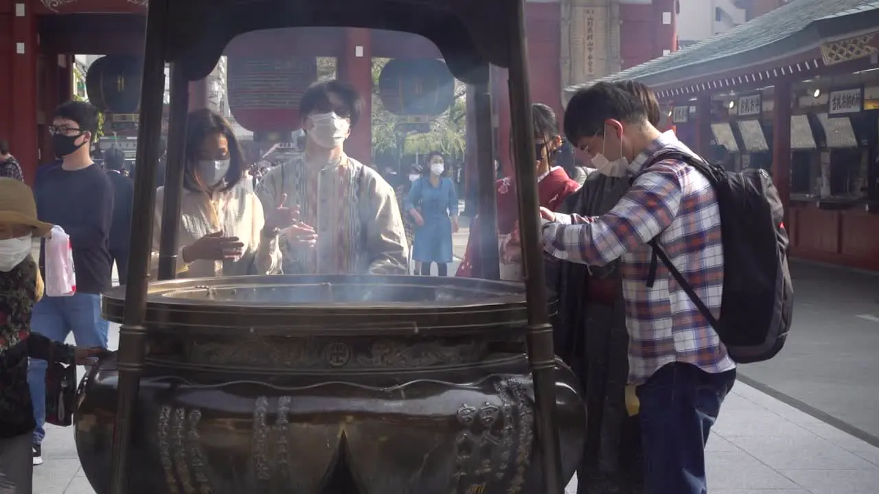 People wearing facemask while cleansing themselves with smoke at Senso-Ji in Japan