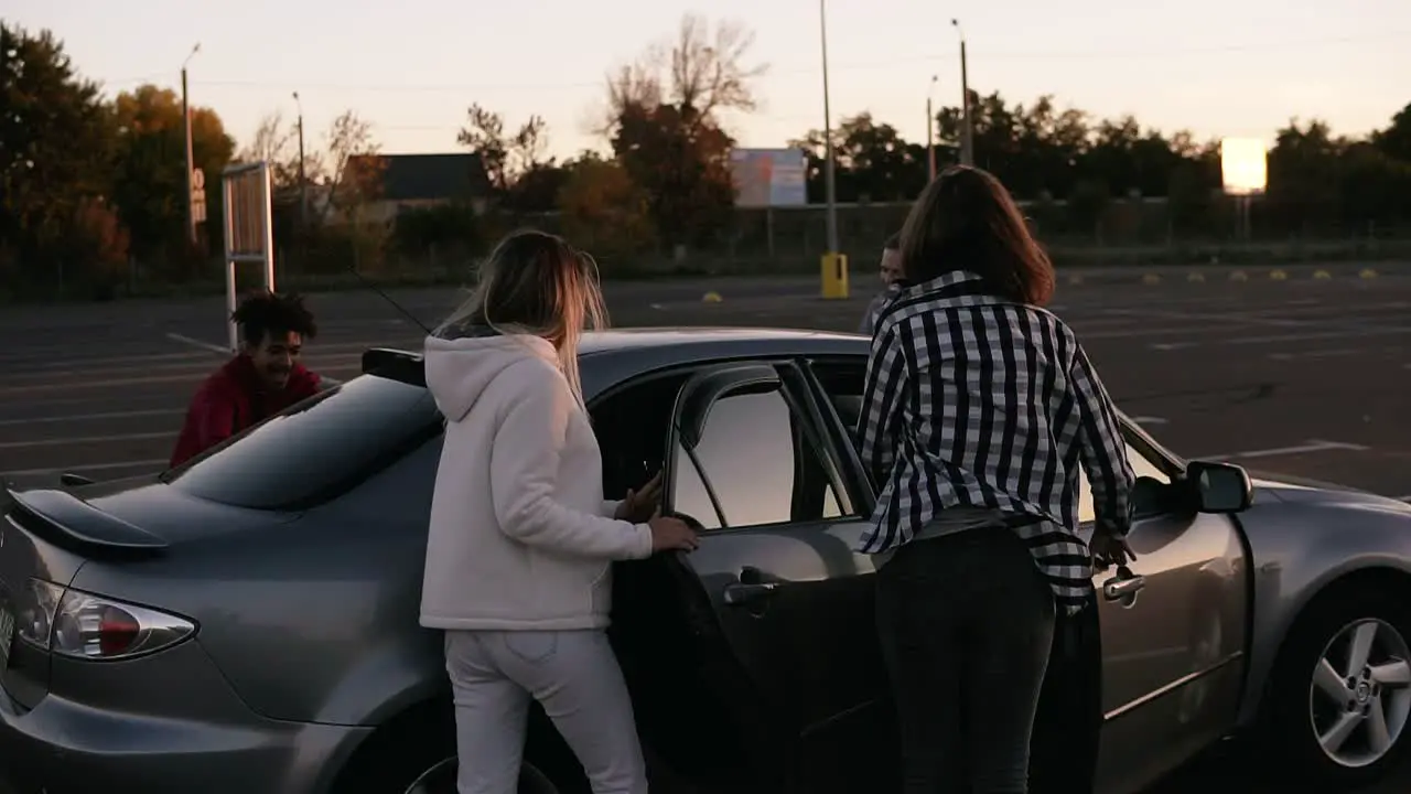 Rare View Of A Multirace Trendy Young Four Friends Are Running By Mall Parking Zone And Sit Into The Silver Coloured Car