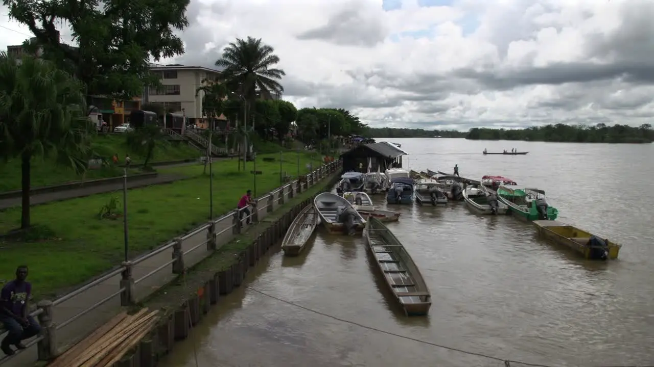 Several river boats docked along the shore of a large river in tropical climate