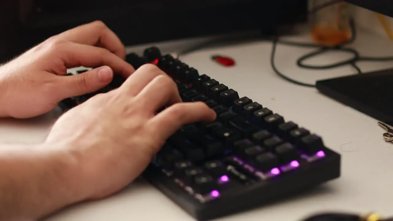 High angle shot of a man’s hands interacting with an rgb keyboard in a dirty computer desk