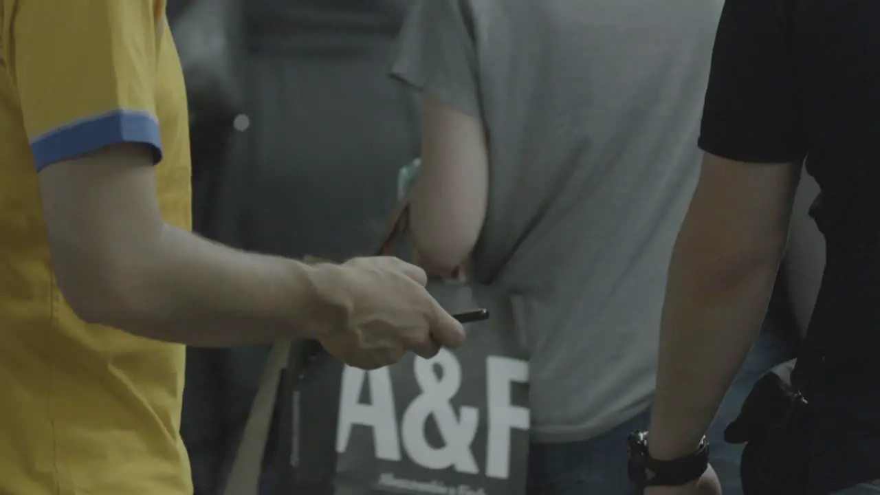 Medium shot handheld footage of people waiting at a subway station focused on individuals using their phones