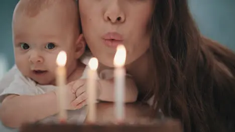 Woman with baby blowing candles on birthday cake Family birthday party