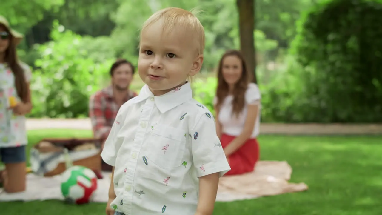 Blonde toddler covering face with hands Family sitting on blanket in park