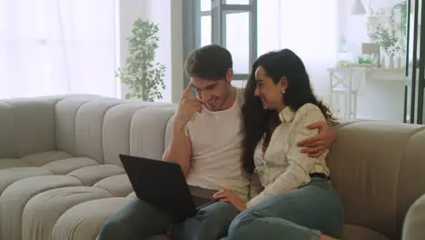 Happy couple watching laptop at home Young man and woman relaxing on sofa