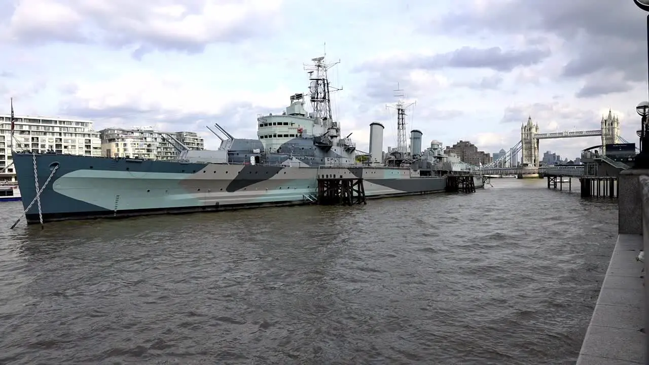 HMS Belfast Slow Motion of A Royal Navy Light Cruiser Docked On River Thames On A Background Of Tower Bridge Under Cloudy Sky In London UK