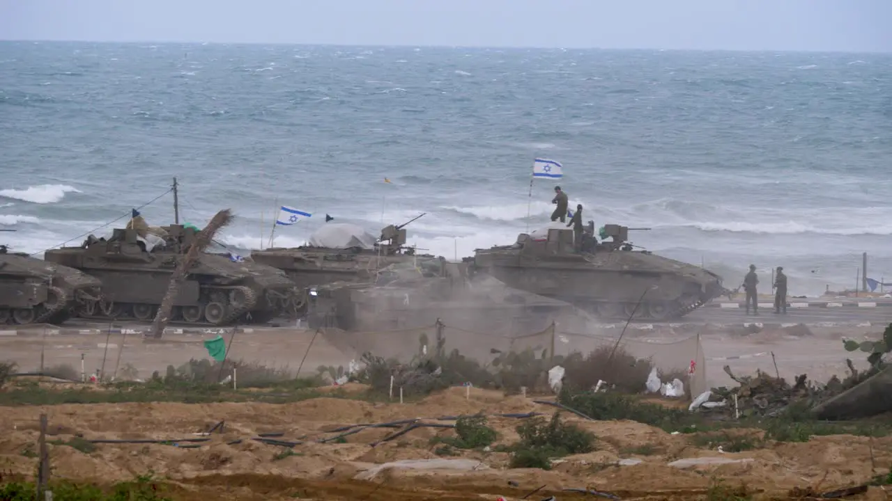 Israeli tank driving past parked tanks on the beach Gaza conflict