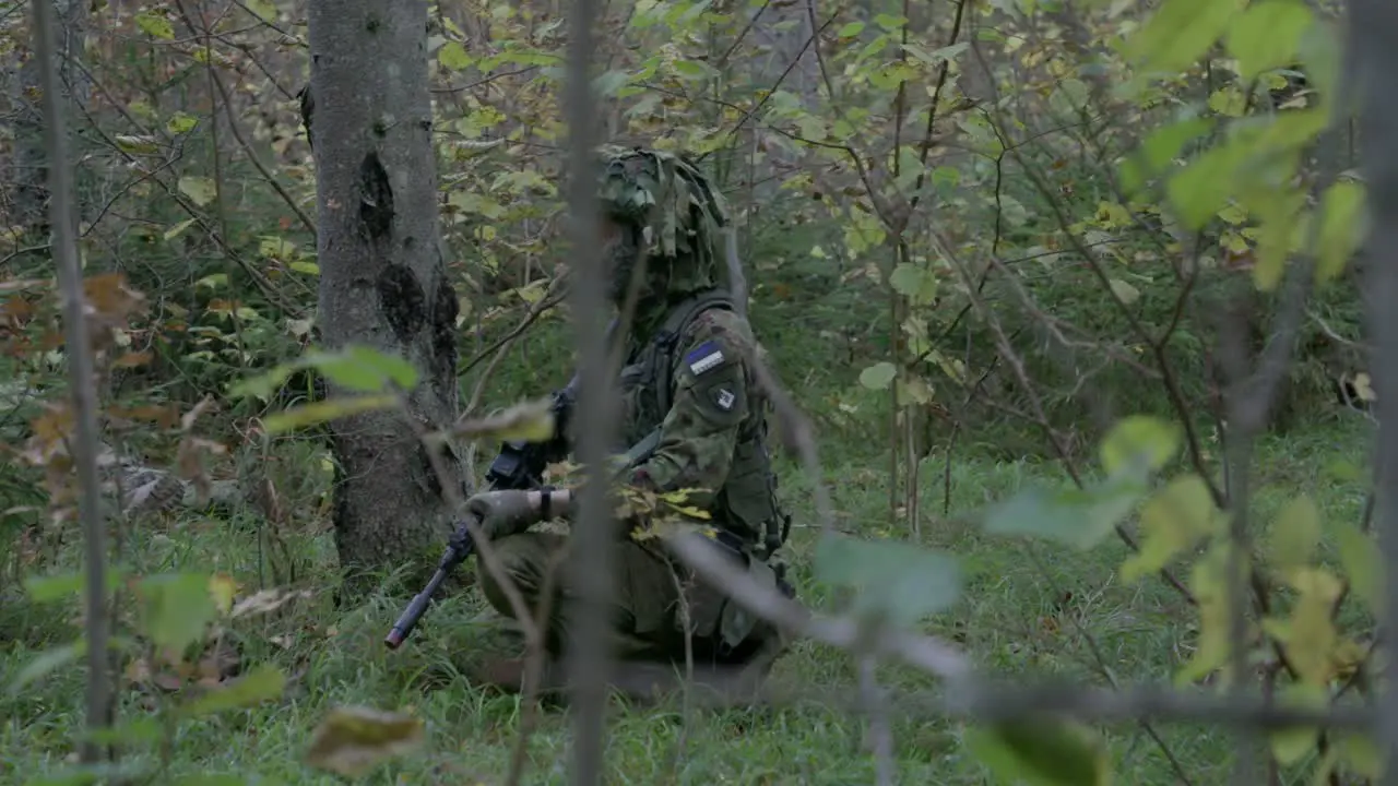 Soldier in camouflage kneel stalking in forest slow motion handheld