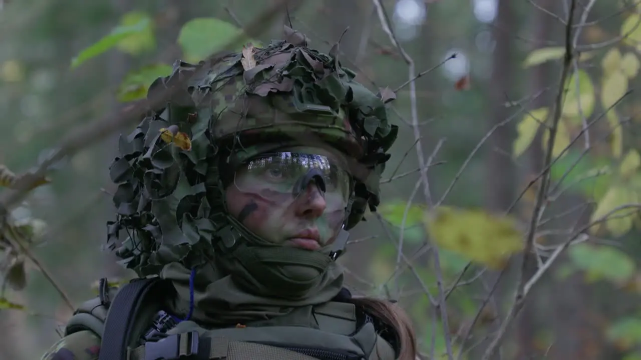 Female soldier in camouflage looking listening in forest closeup handheld