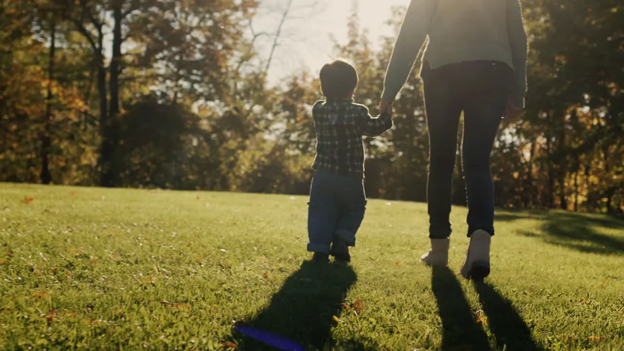 A woman walks with her son in the park leads the baby by the hand