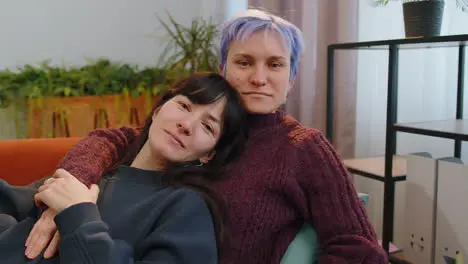 Loving same sex female lesbian women family couple hugging relaxing together lie on sofa at home