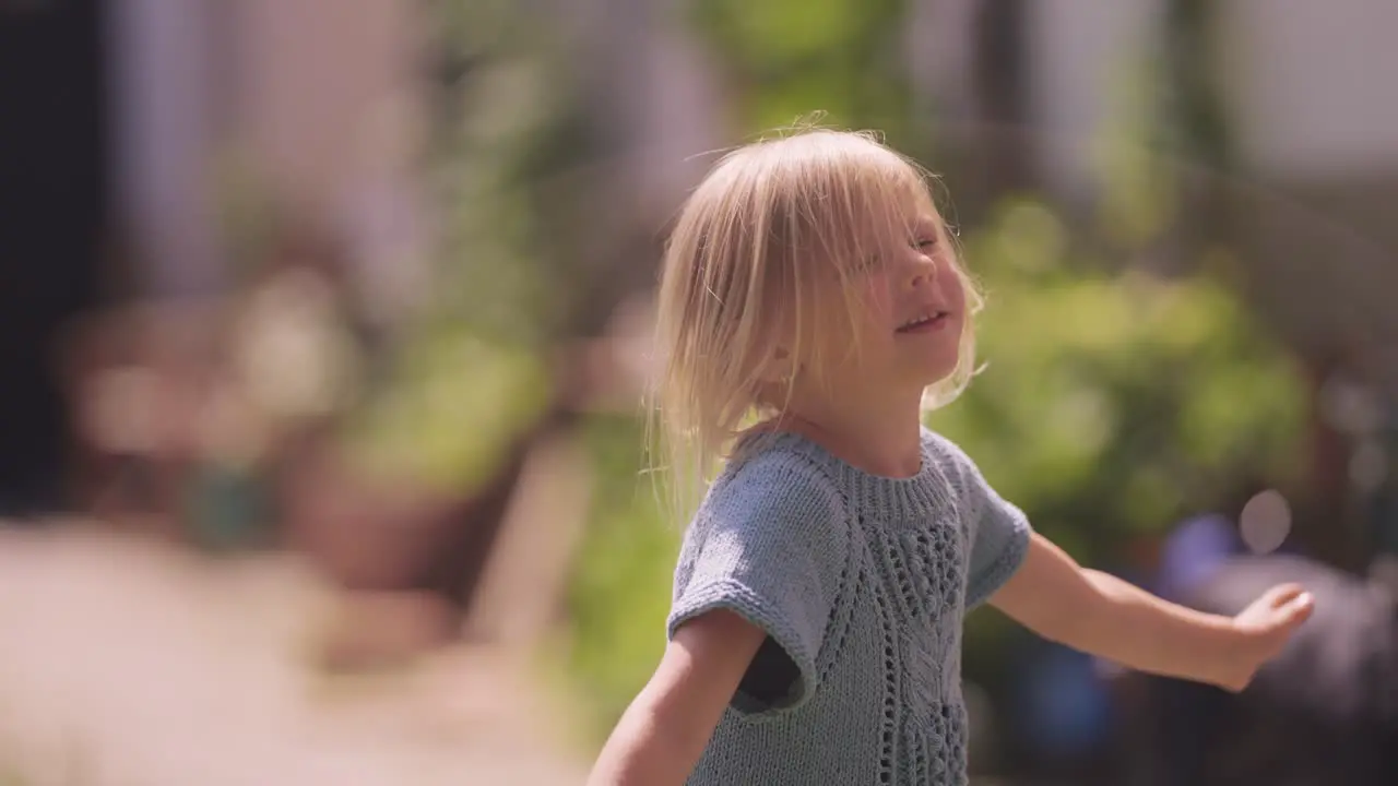 A young blonde girl dances and spins happily in the garden on a sunny day