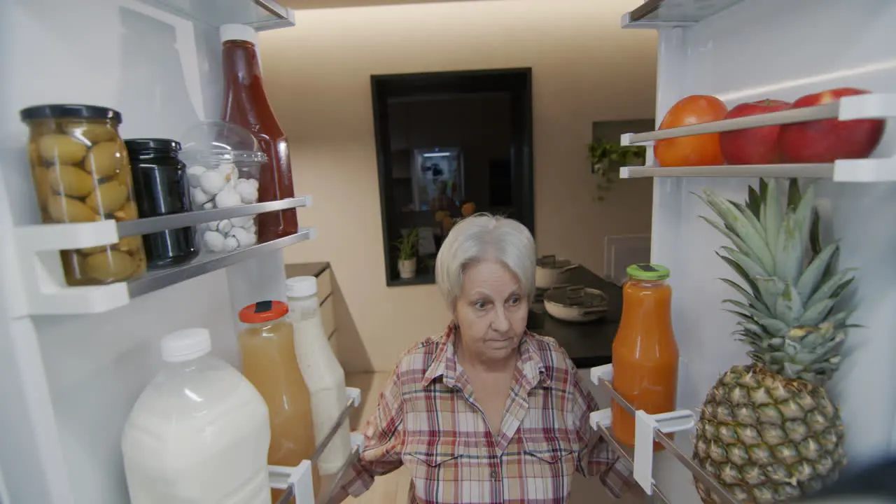 An elderly woman looks into the refrigerator inside view