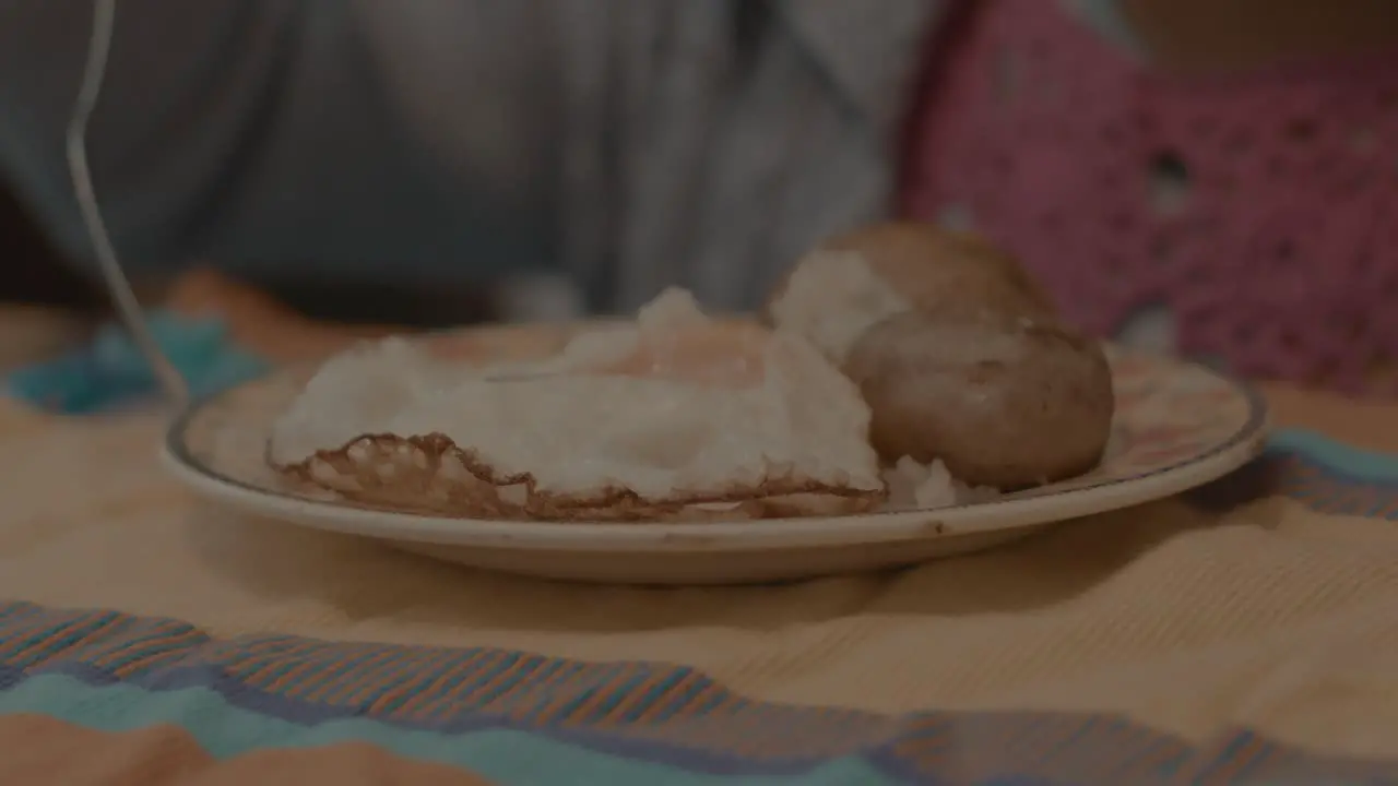 Slow-motion shot of a plate of eggs and potatoes being placed down in front of a child