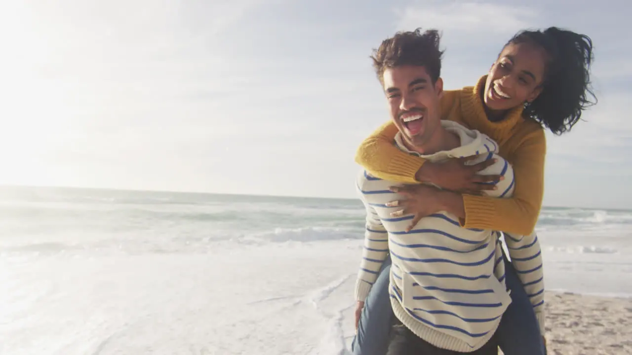 Happy hispanic man carrying piggyback woman and having fun on beach