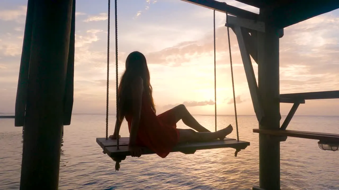 Back view portrait of a girl silhouette swinging at sunset on the beach