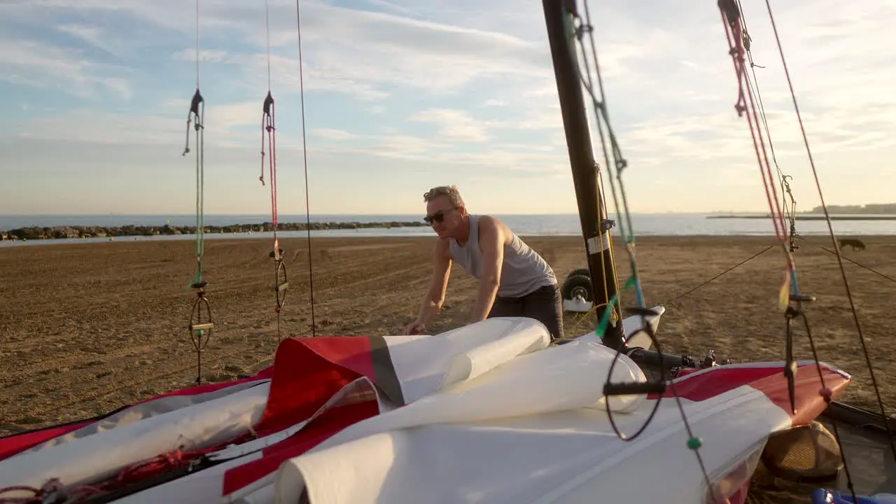 man preparing the sails of a catamaran on the beach in the morning