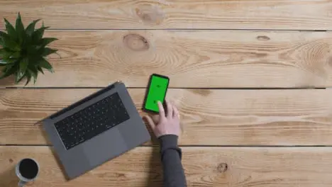 Top Down Shot of Person Working On MacBook with Green Screen Smartphone