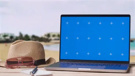 Blue Screen Laptop On Table With Holiday Beach And Hotel In Background