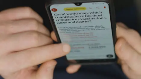 High Angle Close Up of Hands Scrolling On COVID 19 News Website On Smartphone