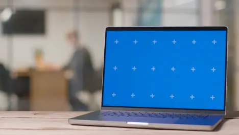 Blue Screen Laptop On Desk In Busy Modern Office