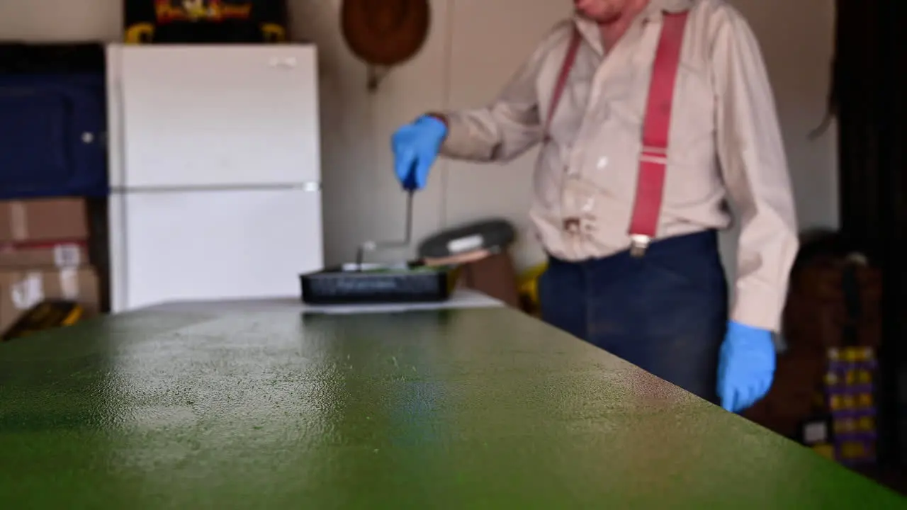 Cropped Image Of A Man Coating Wooden Table Surface With Green Paint Using Roller Brush At The Garage