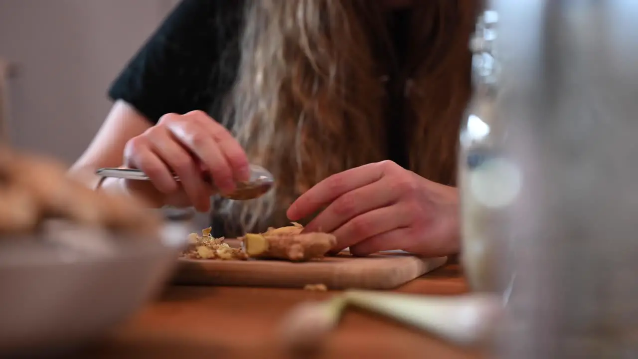 A stationary shot of a woman's hands while peeling ginger with a spoon