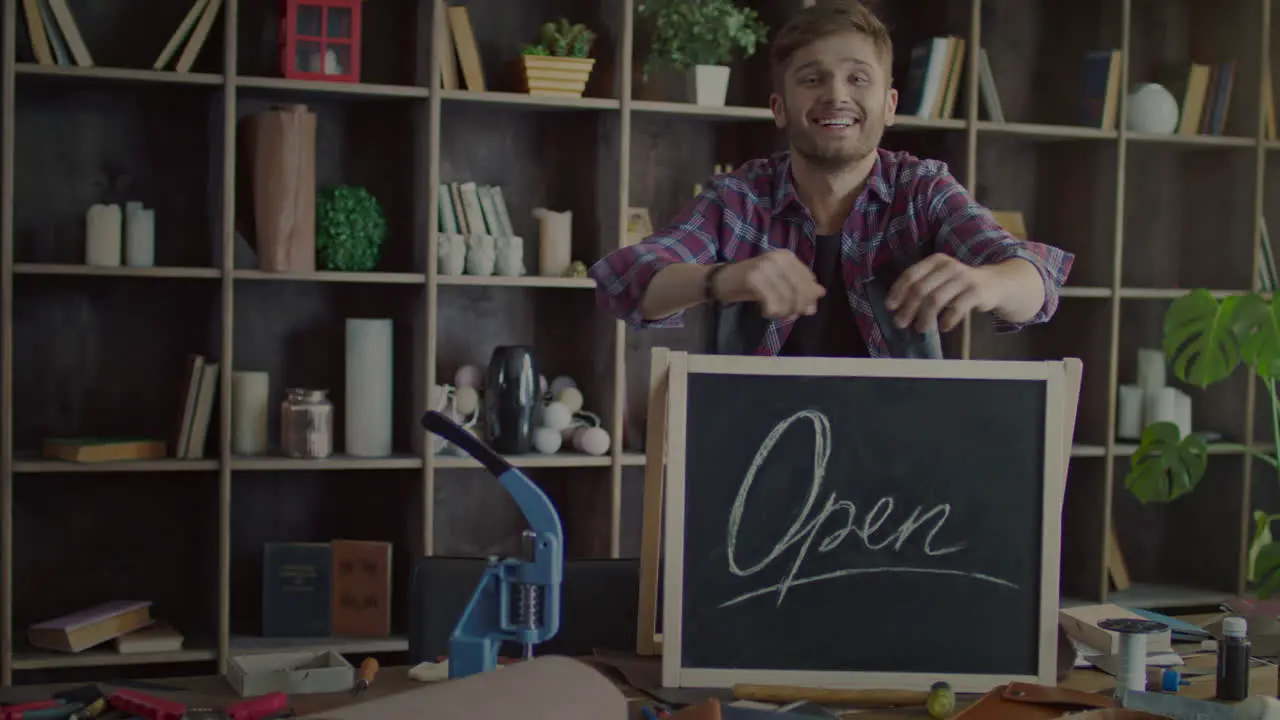 Happy business owner putting open sign on table in small shop