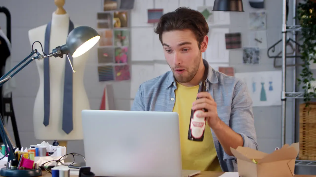 Male Owner Of Fashion Business With Bottle Of Beer Making Video Call On Laptop In Studio