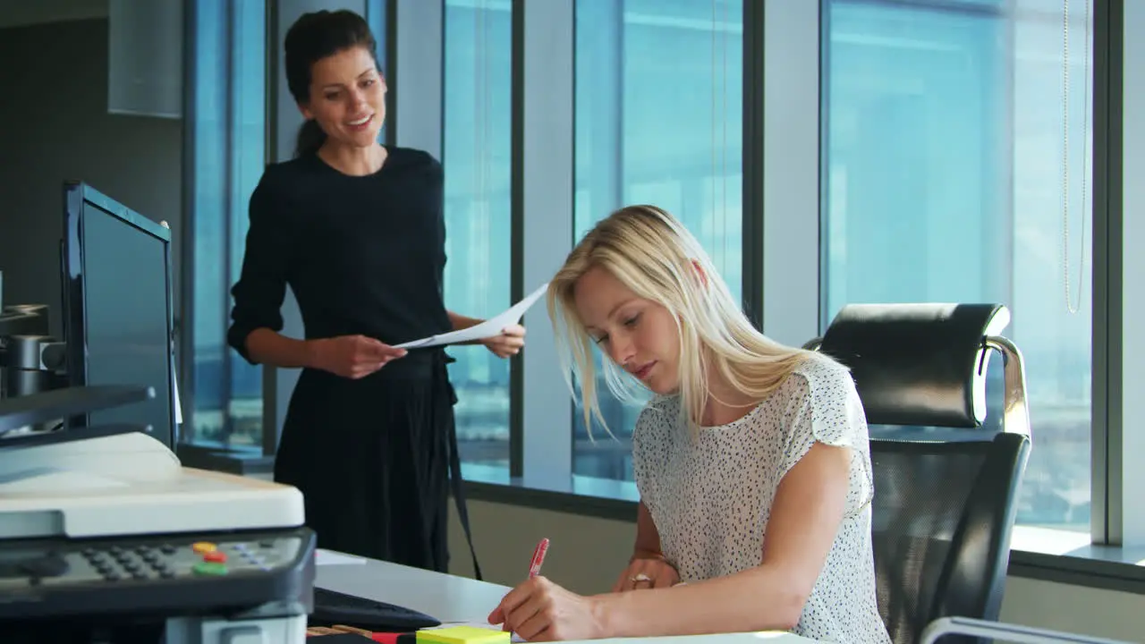 Two Businesswomen Working At Desk Discuss Document