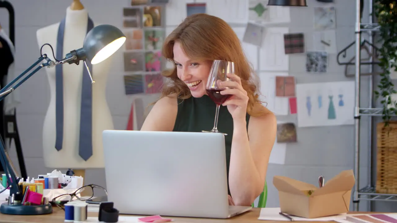 Female Owner Of Fashion Business With Glass of Wine Making Video Call On Laptop In Studio