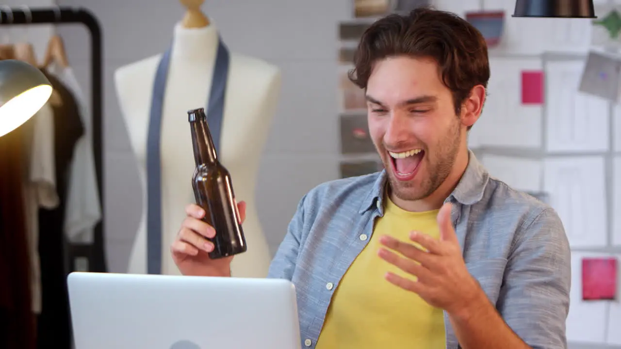 Male Owner Of Fashion Business With Bottle Of Beer Listening To Music On Laptop In Studio