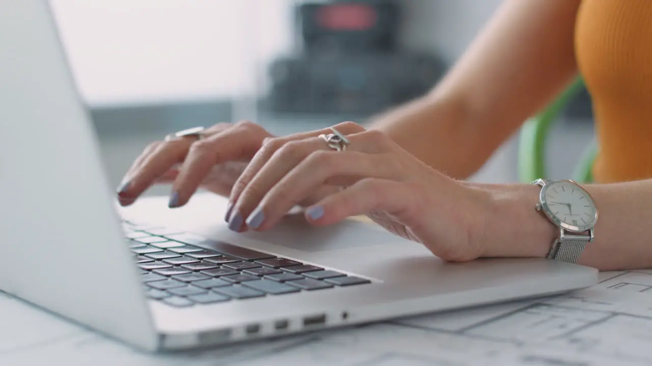 Close Up Showing Hands Of Female Architect In Office Working At Desk On Laptop With Plans